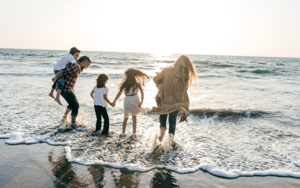 A family walking into a body of water from a sandy shore, sun shining in the background