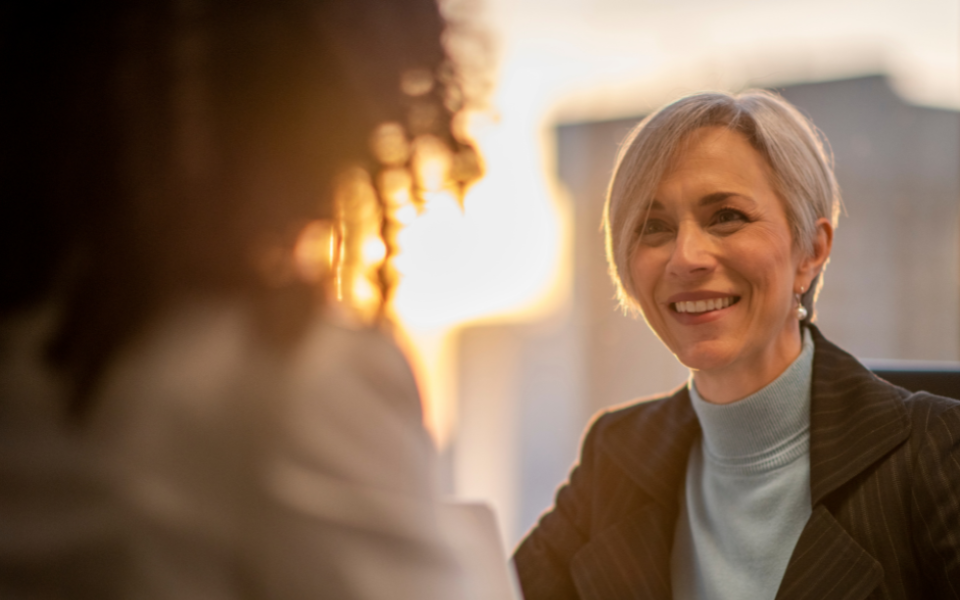 Two women facing one another, one smiling at the other