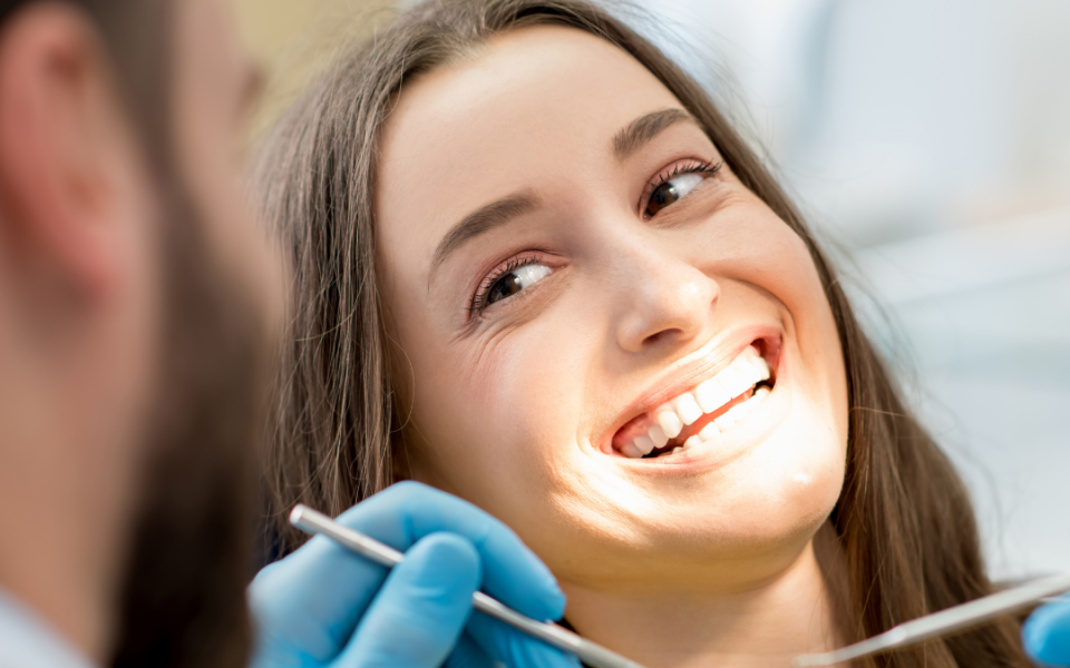 A woman smiling and looking toward a dentist, tools in hands