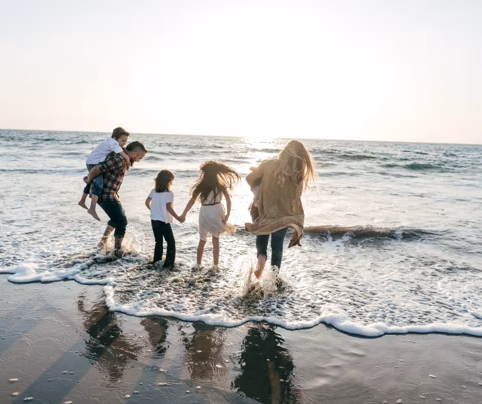 A family walking into a body of water from a sandy shore, sun shining in the background